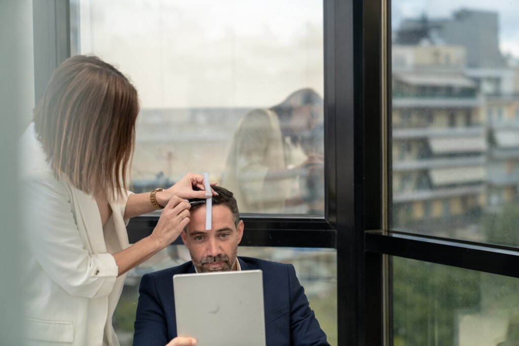 Specialist measuring a man’s hairline during a hair transplant consultation while he checks the design in a mirror.