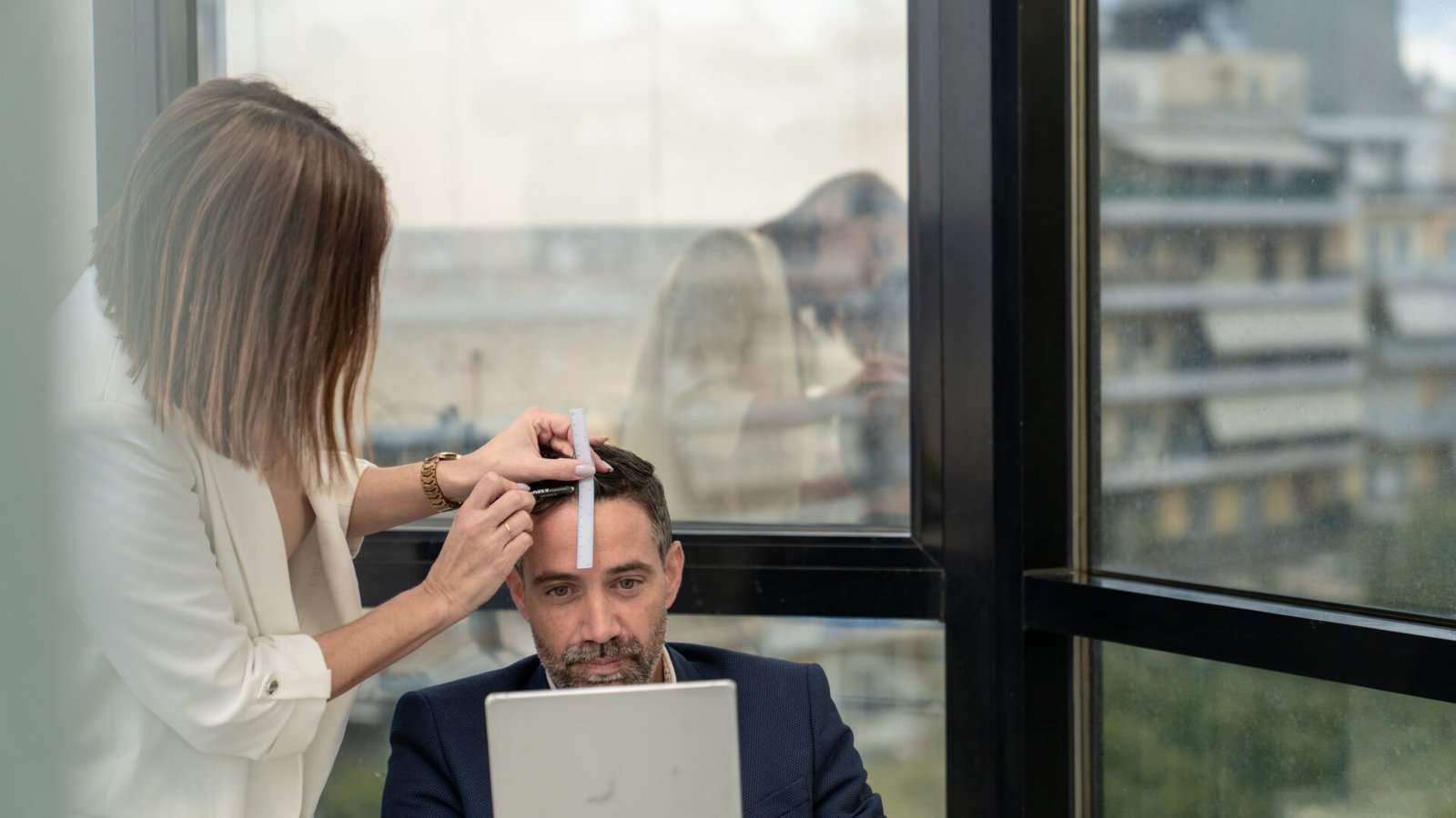 Specialist measuring a man’s hairline during a hair transplant consultation while he checks the design in a mirror.