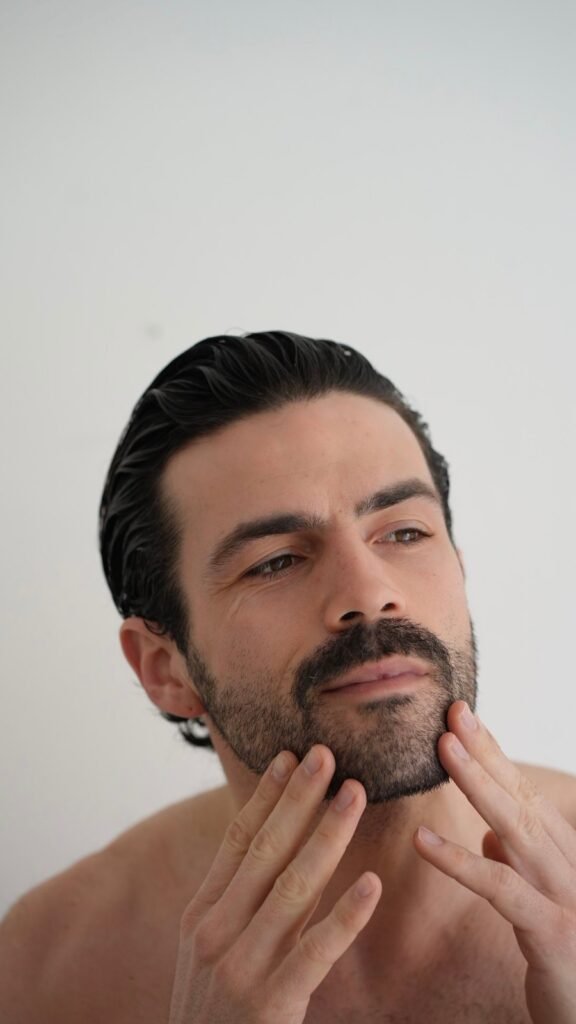 Man touching his beard and jawline while assessing facial appearance and grooming.