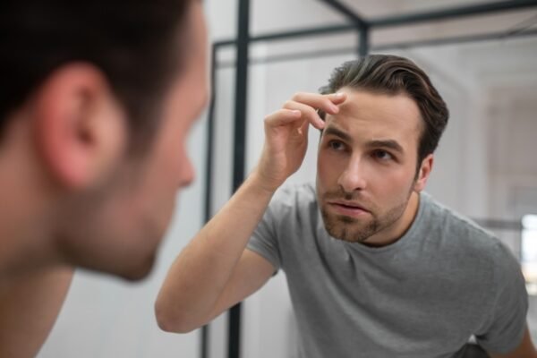 Man examining his frontal hairline in the mirror while checking for early signs of hair loss.
