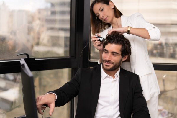 Specialist examining a man’s scalp with magnification during a hair transplant consultation while he looks into a mirror.