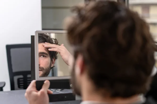 Άνδρας εξετάζει τη hairline του στον καθρέφτη στο πλαίσιο μακροχρόνιας στρατηγικής αντιμετώπισης ανδρικής τριχόπτωσης