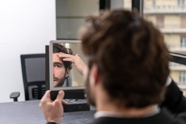 Man checking his frontal hairline in a handheld mirror while looking for signs of thinning.