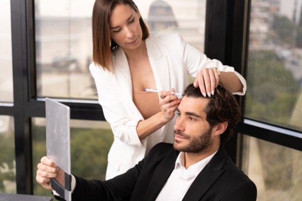 Specialist marking a man’s frontal hairline during a hair transplant consultation while he looks in a mirror.